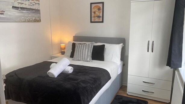 A bedroom with a bed, a nightstand, a wardrobe, and a painting on the wall. - 4BR Sleeps 9 With Garden and Parking (Birmingham)