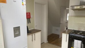 A compact kitchen with a white refrigerator, a stove, and a microwave. There is a fire blanket on the wall and a small window. - 4BR Sleeps 9 With Garden and Parking (Birmingham)