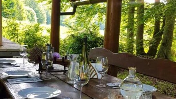 A wooden dining table set outdoors with plates, glasses, and a pitcher.