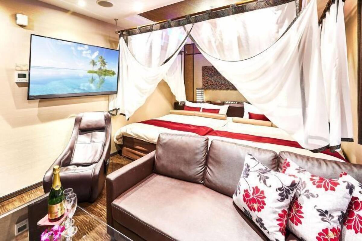 Een slaapkamer met een bed, een massagestoel, een televisie en een fles champagne.