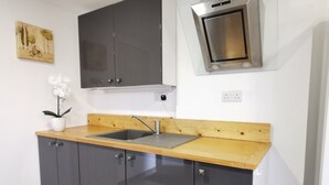 Une cuisine avec des meubles de couleur sombre, un plan de travail en bois, un évier en acier inoxydable et un four fixé au mur.