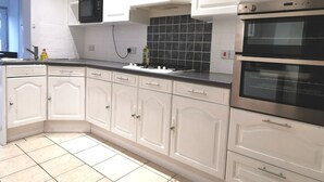 A kitchen with white cabinets, a black tiled backsplash, and stainless steel appliances. - Captivating 6-bed House in Havant With Parking (Havant)