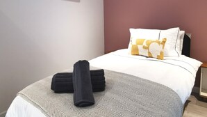 A neatly made bed with a patterned bedspread, a pair of folded towels, and a pillow with a geometric design. - Captivating 6-bed House in Havant With Parking (Havant)