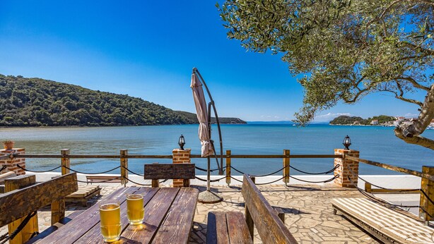 A wooden deck with tables and benches overlooking a lake, with a clear view of the water and distant hills. - Sea View Summer Paradise - Emily 1 (Kampor)