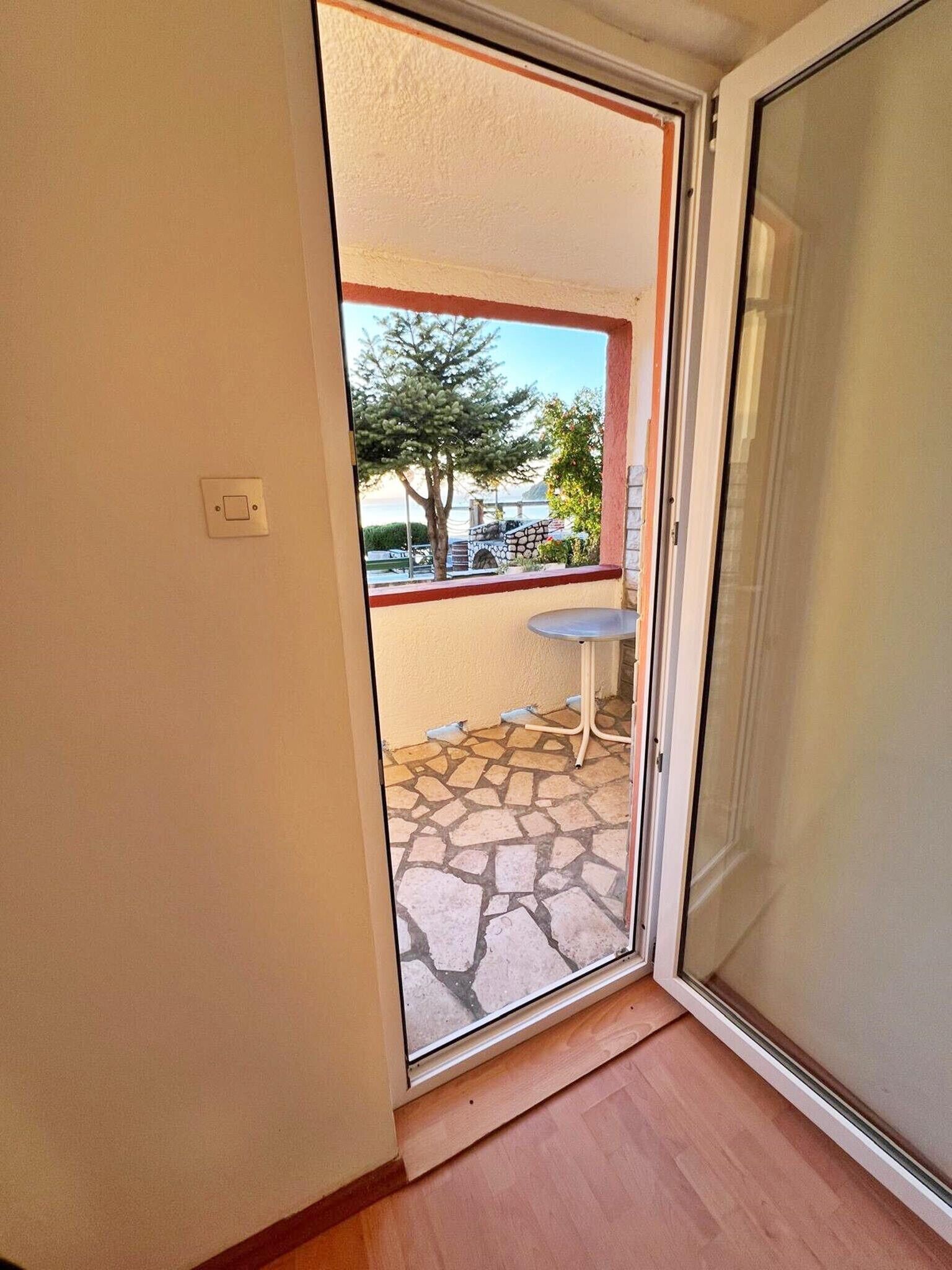 A room with a sliding glass door leading to an outdoor patio with a stone floor, a small table, and a tree.