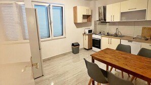 A modern kitchen with white cabinets, a microwave, and a sink. There is a dining table with chairs and a trash can. - Sea View Summer Paradise - Emily 1 (Kampor)