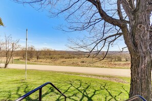 A grassy area with a metal railing, a tree, and a dirt road in the background. - Cozy Conesus Vacation Rental Near Wineries & Lake! (Conesus)