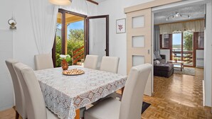 A dining area with a table set for four, a white lace tablecloth, and a view of the outdoors through a glass door. - Anamar- Three bedroom Apartment with Sea View (Supetarska Draga)
