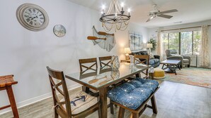 Een eethoek met een glazen tafel, houten stoelen, een kroonluchter en een plafondventilator.