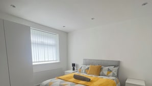 Un dormitorio con una cama, una mesita de noche y un radiador. Cuenta también con una ventana con persianas.