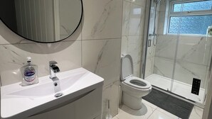 Un baño moderno con un lavabo de mármol blanco, un espejo redondo, un inodoro y una ducha con mampara de vidrio.