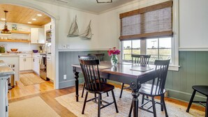 A dining area with a wooden table, four chairs, and a vase with flowers. There is a window with blinds and a view of the outdoors. - Unique Tangier Cottage w/ Chesapeake Bay Views! (Tangier)