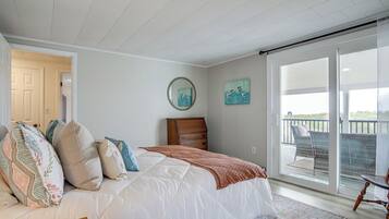 A bedroom with a large bed, a dresser, and a view of a balcony.