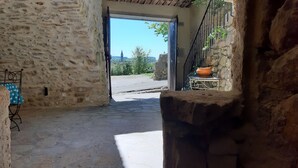 Interior rústico de piedra con un vano que da al exterior, una mesa de piedra con una olla y una silla de metal con mantel de estampado de estrellas.