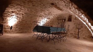 Un interior rústico de piedra con una mesa dispuesta para comer, sillas de metal y un candelabro.