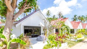 A white building with a large window and a door, surrounded by tropical plants and palm trees. - Bungalow - Sleeps 2 - Terrace - Beach Close (Koh Lan)