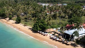 An aerial view of a beach with palm trees, a sandy shore, and buildings in the background. - Bungalow - Sleeps 2 - Terrace - Beach Close (Koh Lan)