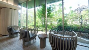 Un interior moderno con tres sillas únicas y una jardinera central, grandes ventanales que ofrecen vistas a un jardín ajardinado.