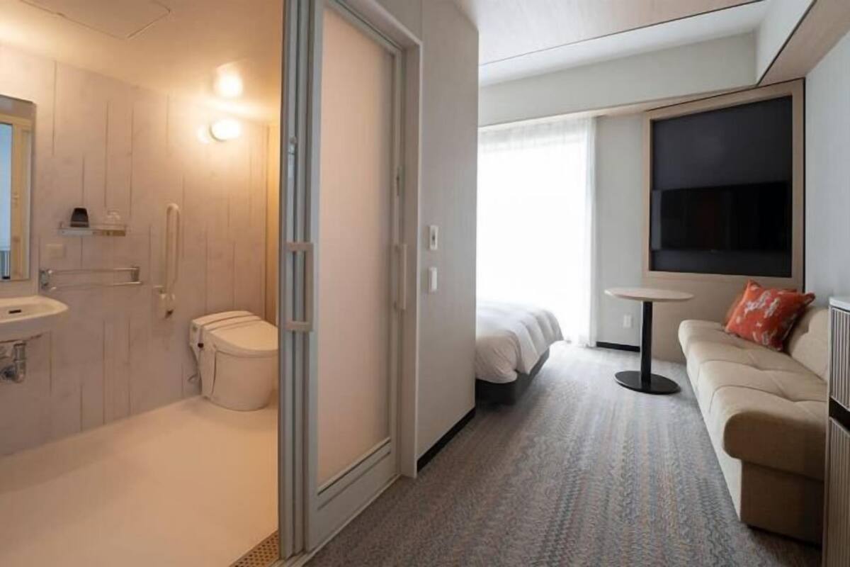 A hotel room with a bathroom, a bed, a sofa, and a TV.