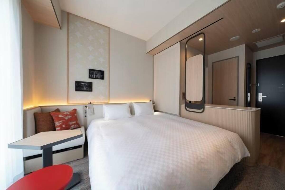 A modern hotel room with a large bed, a small table, a sofa, and a mirror.