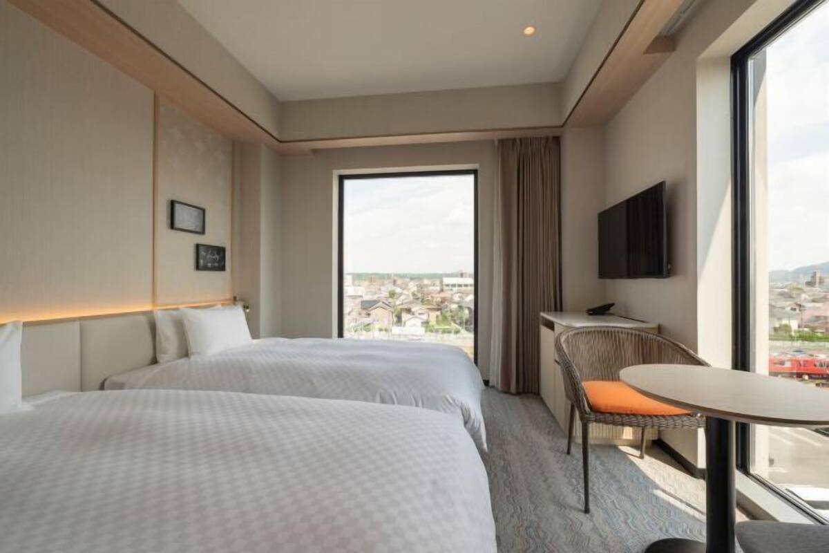A hotel room with two beds, a TV, a balcony with a view, and a small table.