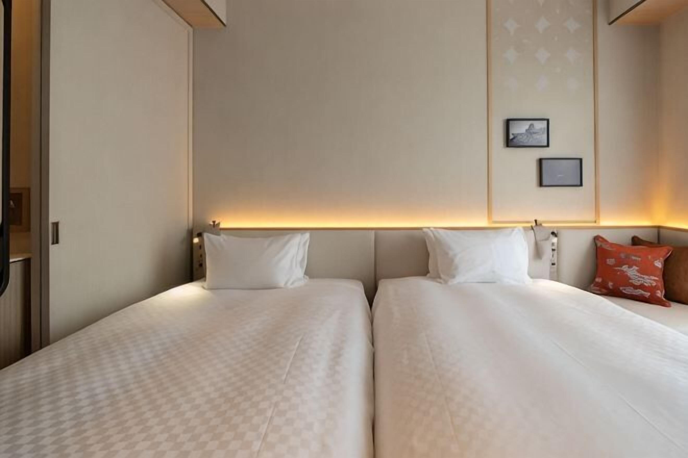 Quarto de hotel com duas camas, cabeceira com luz e quadro pendurado na parede.