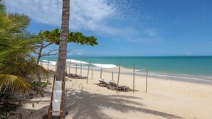 A beach with white umbrellas, lounge chairs, and a wooden walkway. - Fazenda São Francisco do Corumbau (Prado)