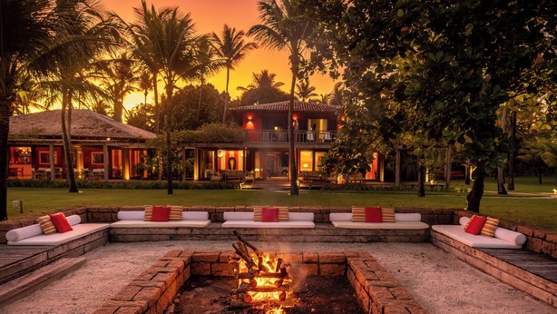 A courtyard with a fire pit, outdoor seating, and a building with a balcony. - Fazenda São Francisco do Corumbau (Prado)