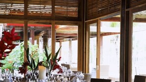 A dining area with wicker chairs, a wooden table set for a meal, and large windows allowing natural light. - Fazenda São Francisco do Corumbau (Prado)