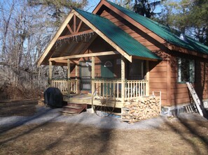 A wooden cabin with a green roof, a porch with steps, and a wheelbarrow filled with firewood. - Cozy Camp Retreat! Enjoy four wheeling, hunting, 3 miles to Redfield Reservoir. (Redfield)