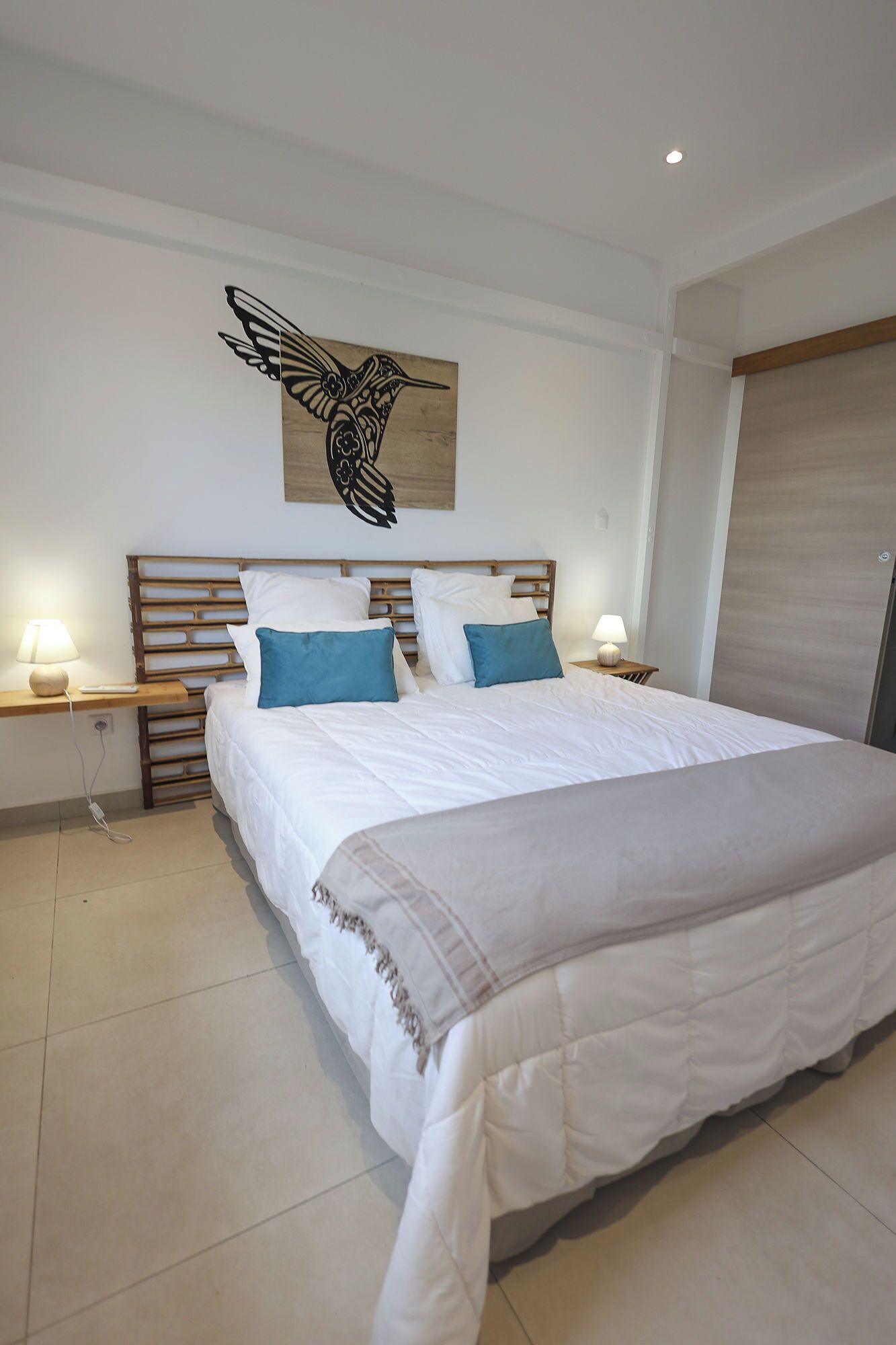 A bedroom with a large bed, two bedside tables with lamps, a wooden headboard, and a wall-mounted artwork of a bird.