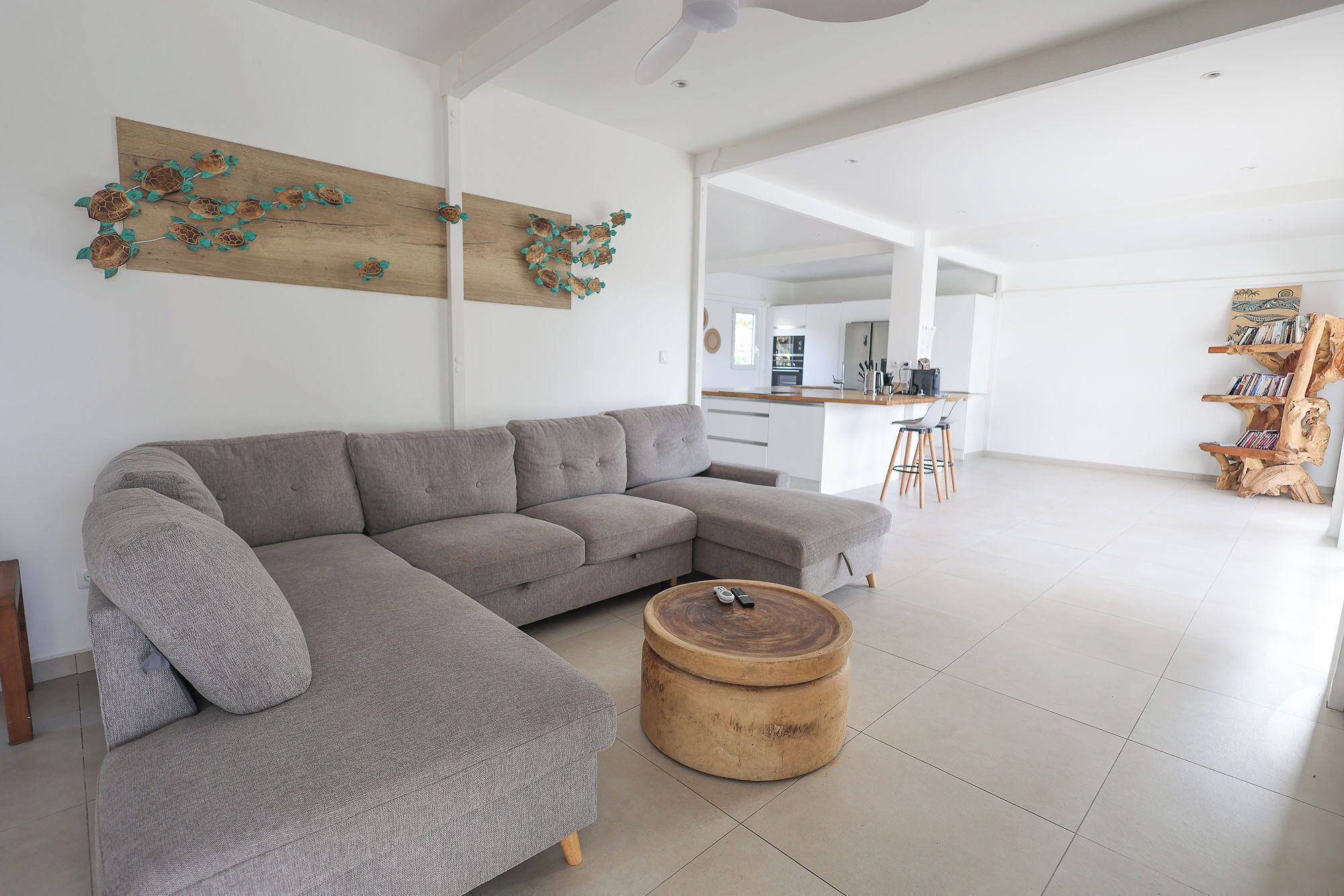 Un salon spacieux avec un grand canapé d’angle gris, une table basse ronde en bois et une œuvre d’art murale en bois.