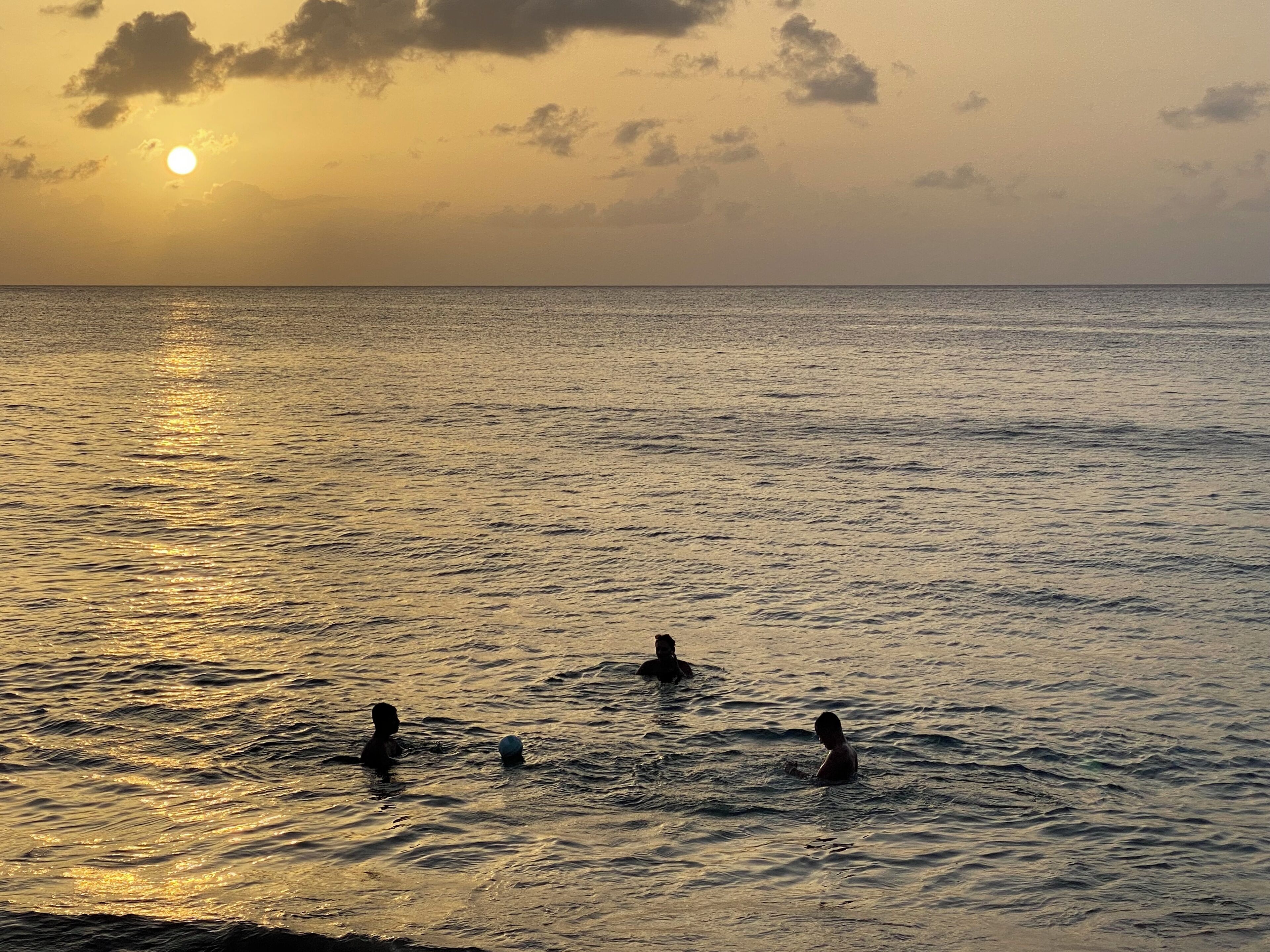Pôr do sol sobre um mar calmo, com pessoas nadando.