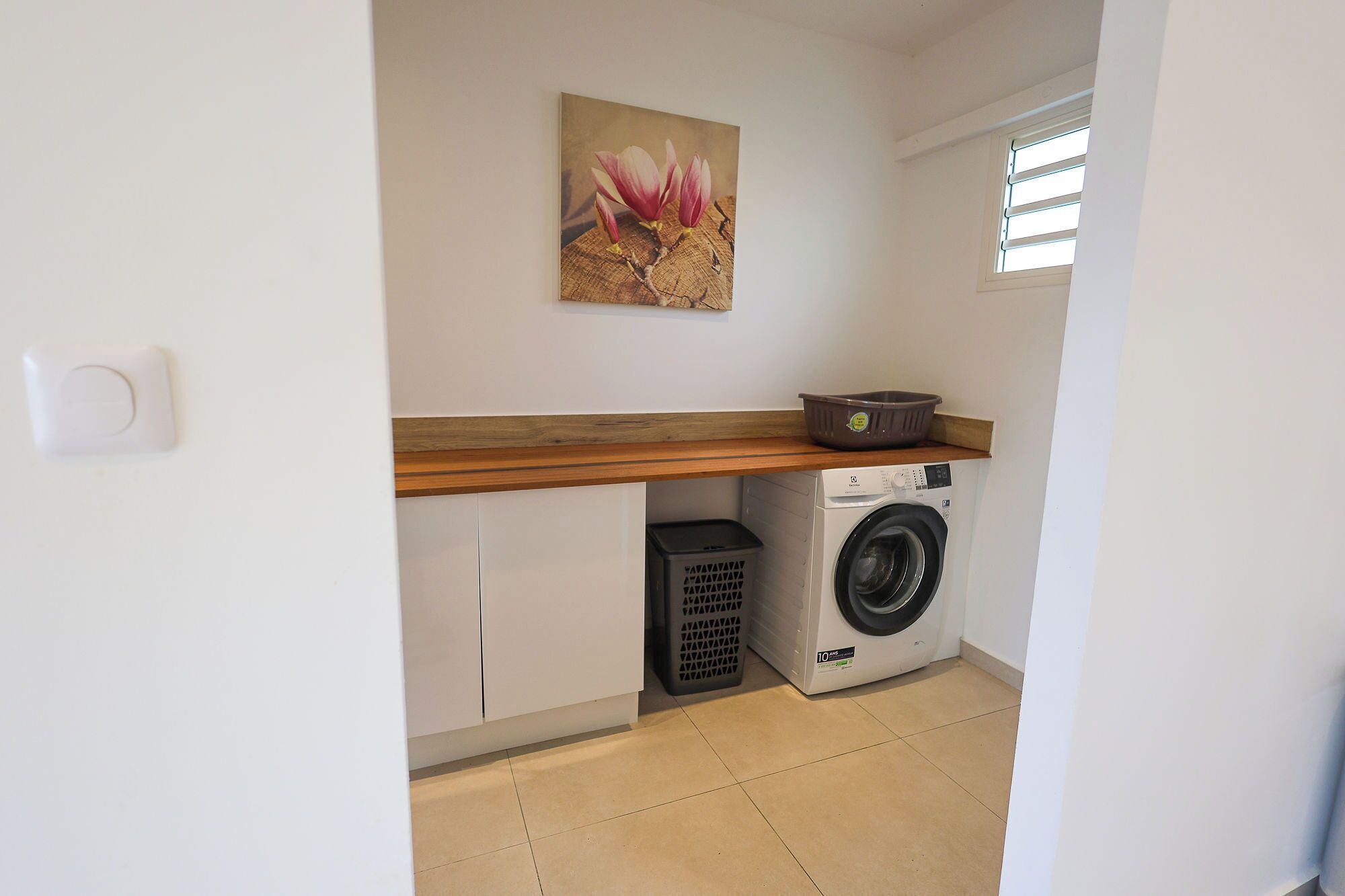 A laundry room with a washing machine, a drying rack, and a trash bin.
