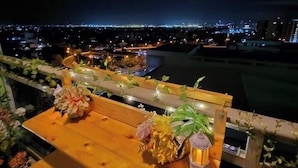 A balcony with a wooden table and chairs, decorated with flowers and a lantern. A cityscape is visible in the background. - Azure Staycation by Siaos (Parañaque)