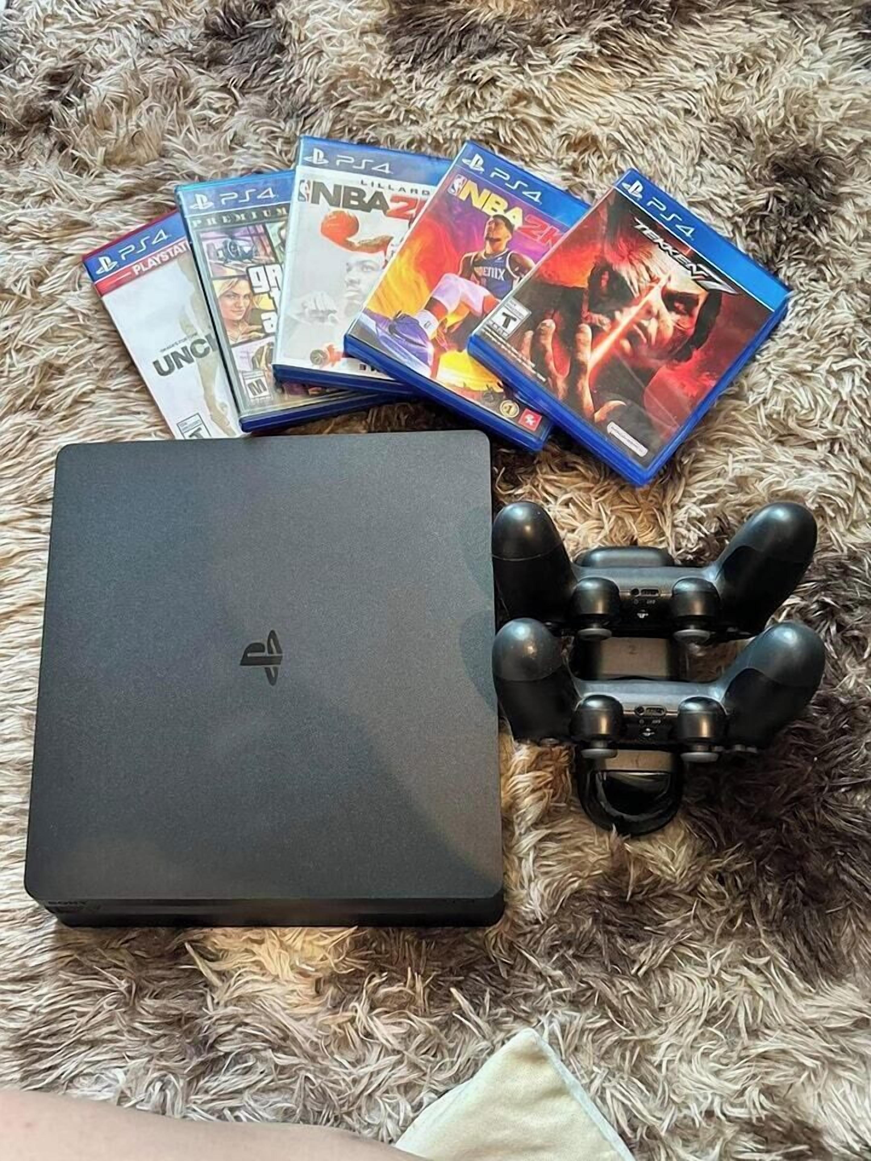 A laptop, a PlayStation controller, and several PlayStation game cases on a textured surface.