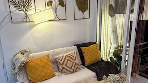 A modern living room with a sofa, decorative wall art, a glass coffee table, and a view through a glass door. - Azure Staycation by Siaos (Parañaque)