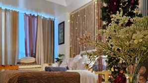 A bedroom with a bed, a bedside table with a candle, a vase with flowers, and a shower area. - Azure Staycation by Siaos (Parañaque)
