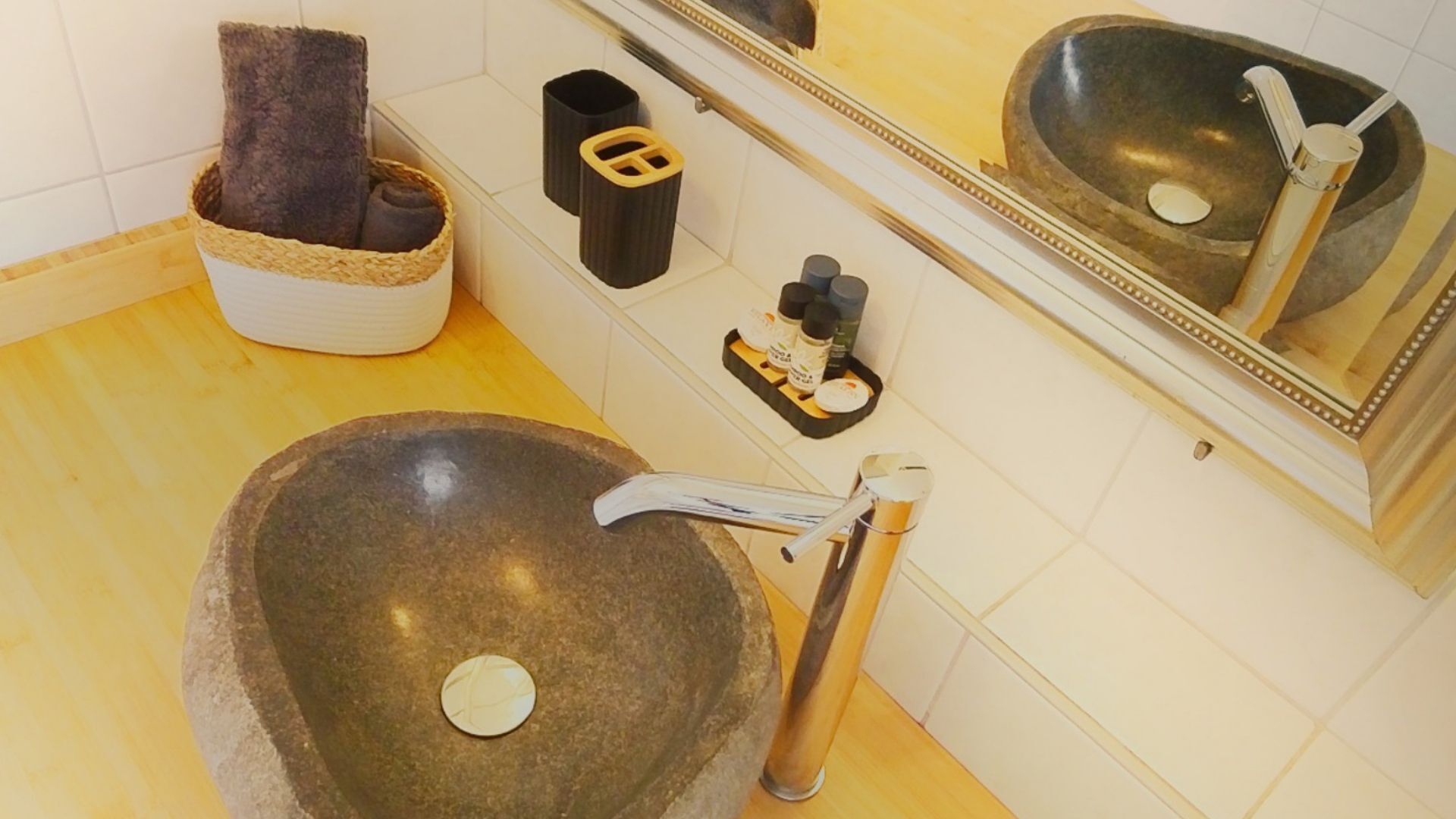 Une salle de bain avec un grand lavabo en pierre, un porte-serviettes, une poubelle et un miroir au-dessus du lavabo.