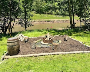 A garden area with a fire pit, logs, and a barrel.