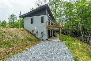 Una casa moderna de dos pisos con balcón, camino de grava y fondo boscoso.