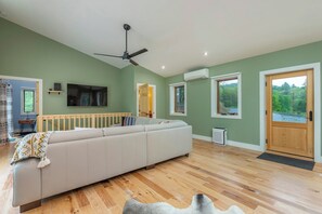 A modern living room with a sectional sofa, a ceiling fan, and a large window with a view of greenery. - Mtn Retreat, River Access, Fire Pit, WiFi, Grill! (Spruce Pine)