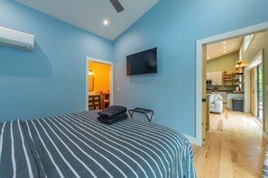 Ein Schlafzimmer mit Bett, Fernseher und Klimaanlage. Blick auf eine Küche und einen Essbereich.