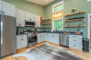 A modern kitchen with white cabinets, stainless steel appliances, and wooden shelves.