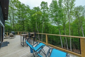 A wooden deck with outdoor furniture, a pool, and a view of a forested area.
