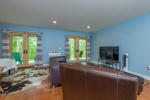 A living room with a brown leather sofa, a television, and a large window with patterned curtains.