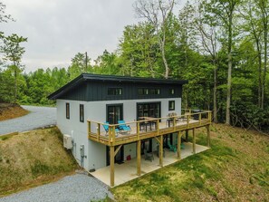 A modern two-story house with a balcony, a covered patio, and a gravel driveway.