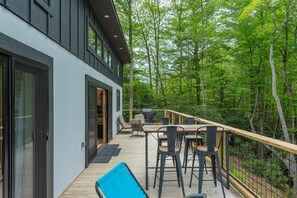 A modern house with a deck, outdoor furniture, and a forested backdrop.