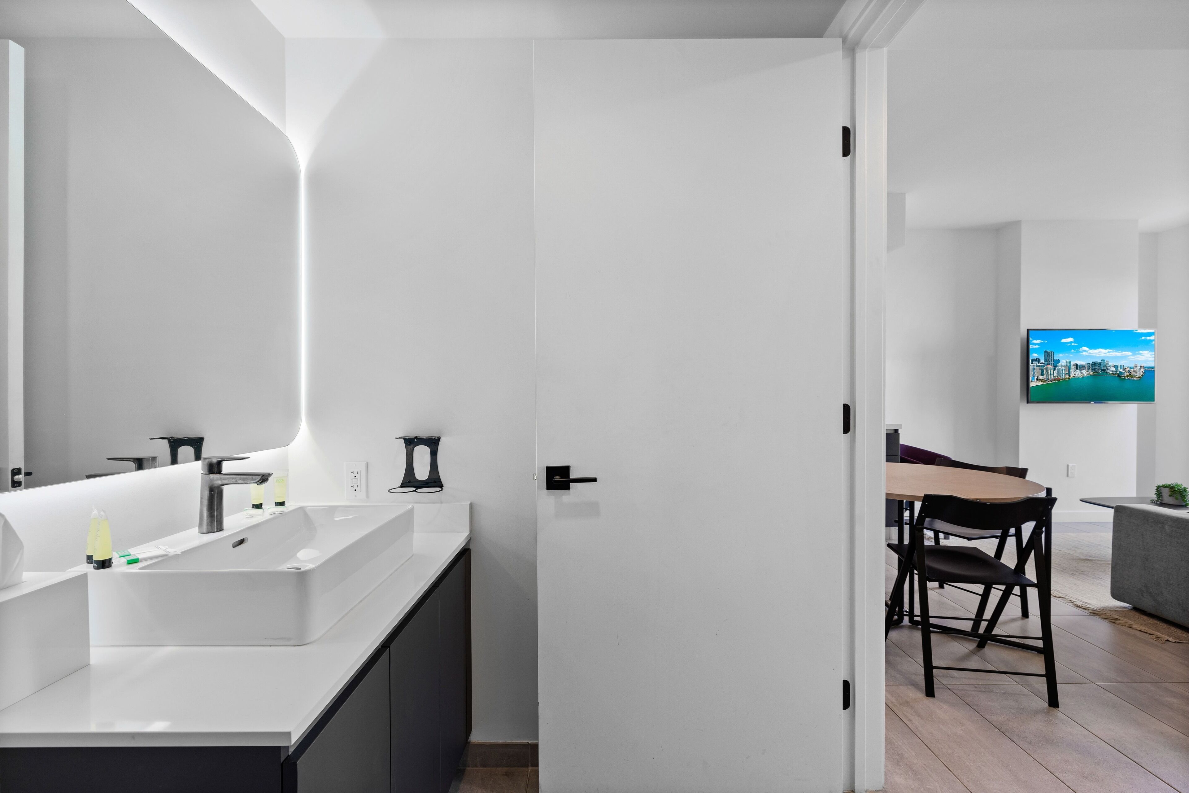 Een moderne badkamer met een grote spiegel, een wit wastafelmeubel en zwarte kastjes.