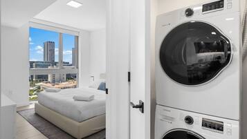 Habitación de hotel moderna con una cama grande, lavadora y vistas de la ciudad a través de amplias ventanas.